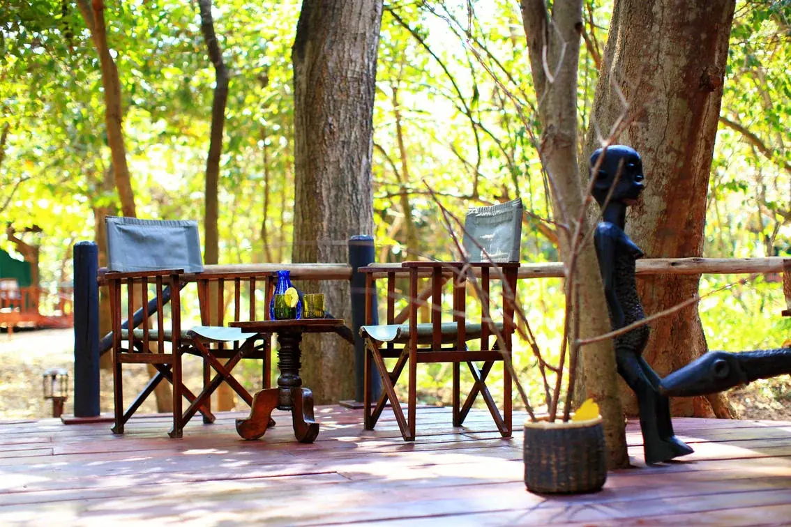 Forest-shaded seating deck at Mbali Mbali Gombe Tented Camp with African wood carvings