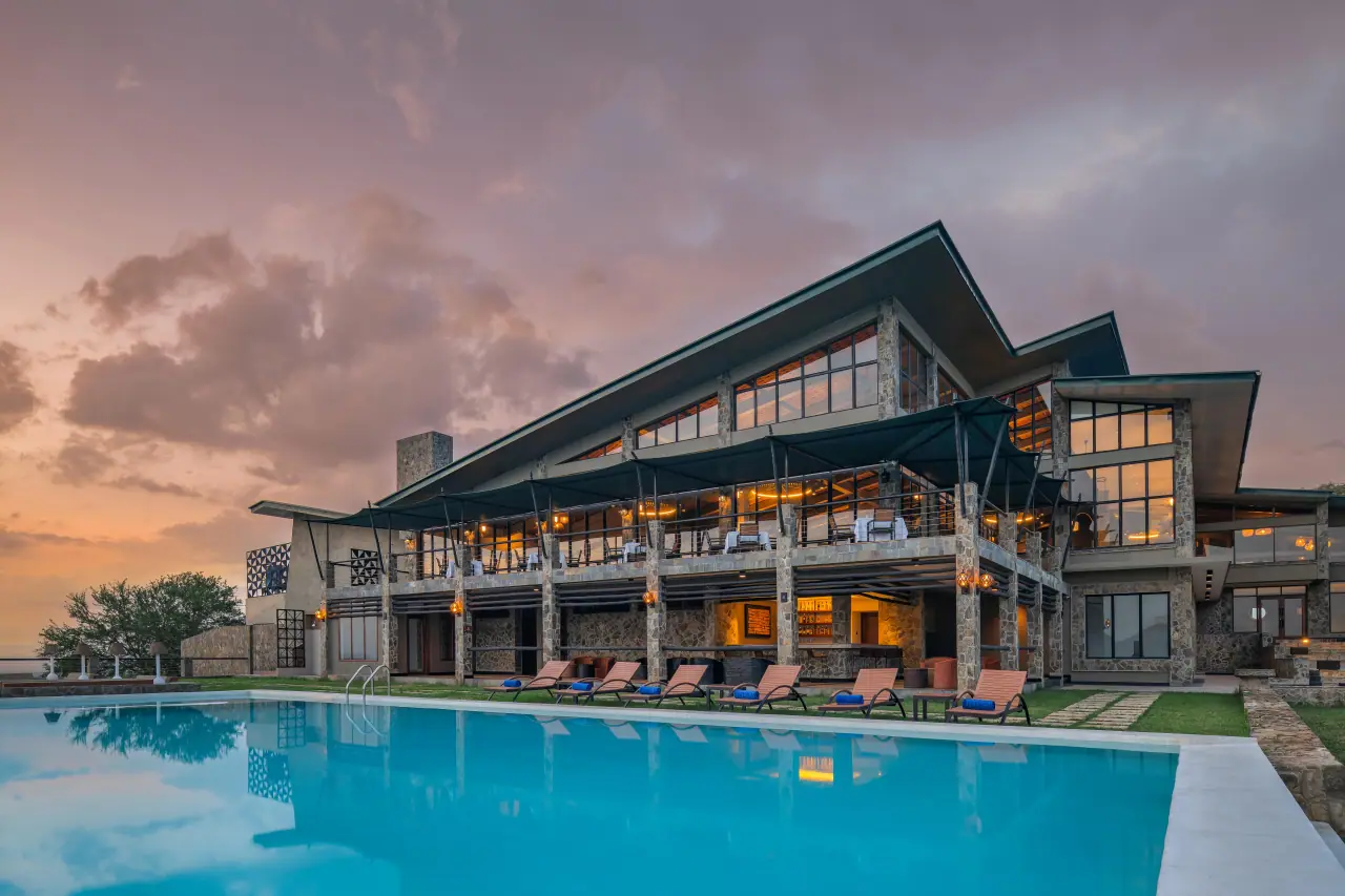 Mikumi Wildlife Lodge's stone-and-glass main building and swimming pool lit at dusk