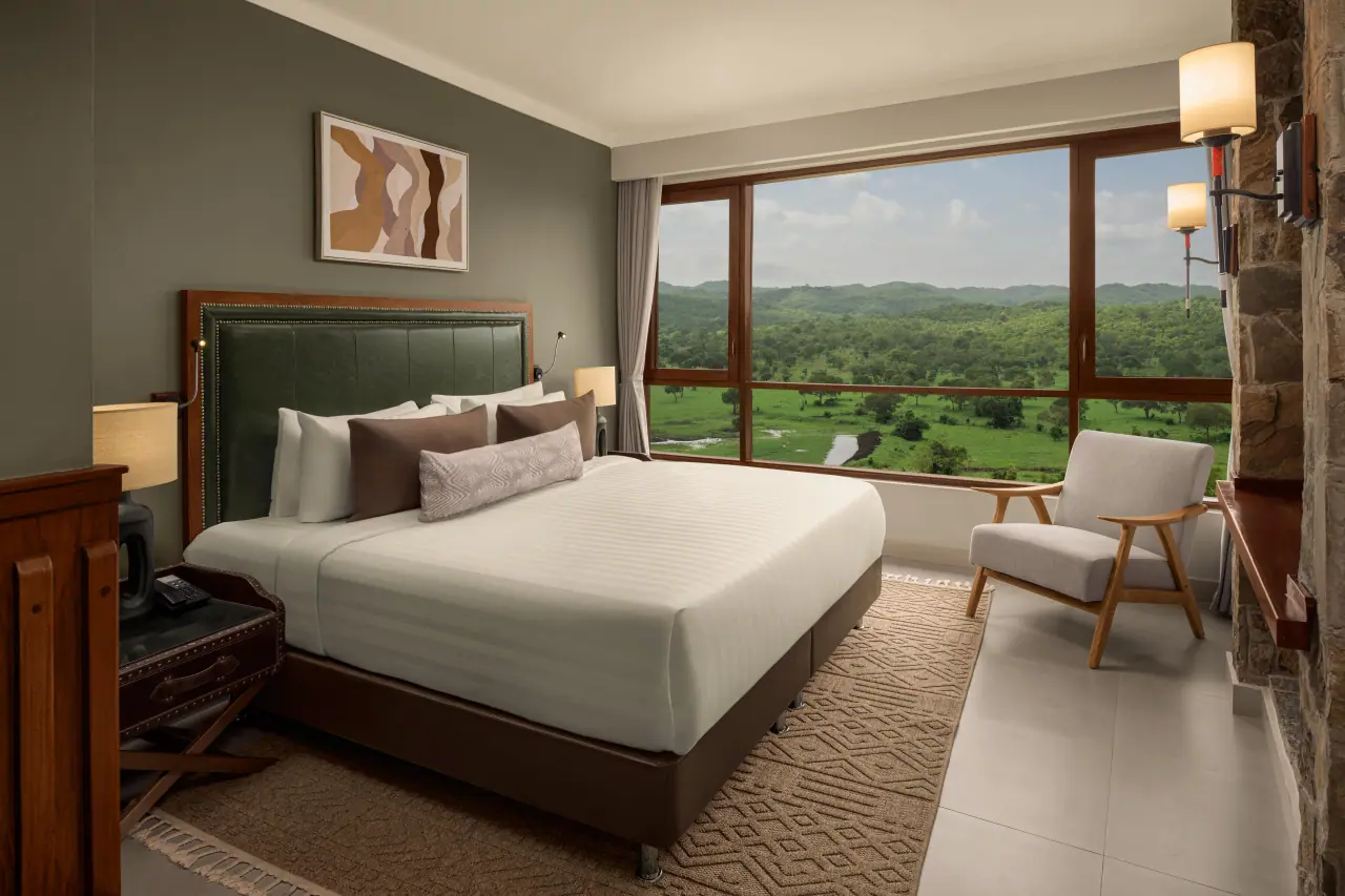 Guest room at Mikumi Wildlife Lodge with a king bed and floor-to-ceiling windows overlooking the floodplain