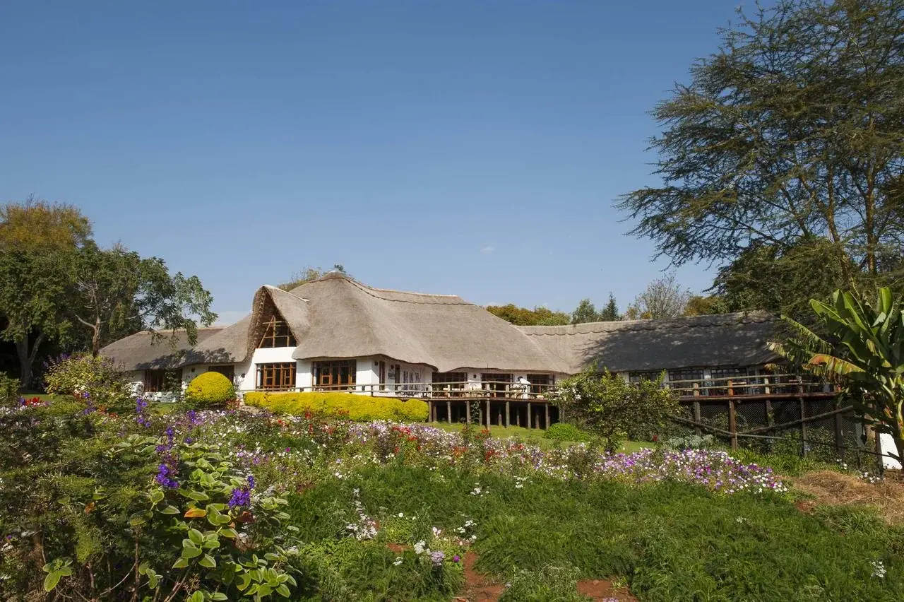 Thatched-roof main building at Ngorongoro Farm House seen across its flower gardens