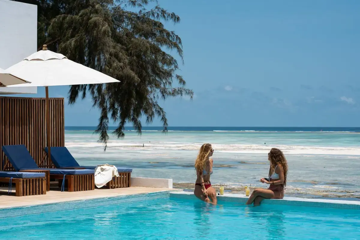 Two guests relaxing on the edge of the infinity pool at Nungwi Dreams By Mantis, overlooking the turquoise reef waters of Zanzibar's northern tip