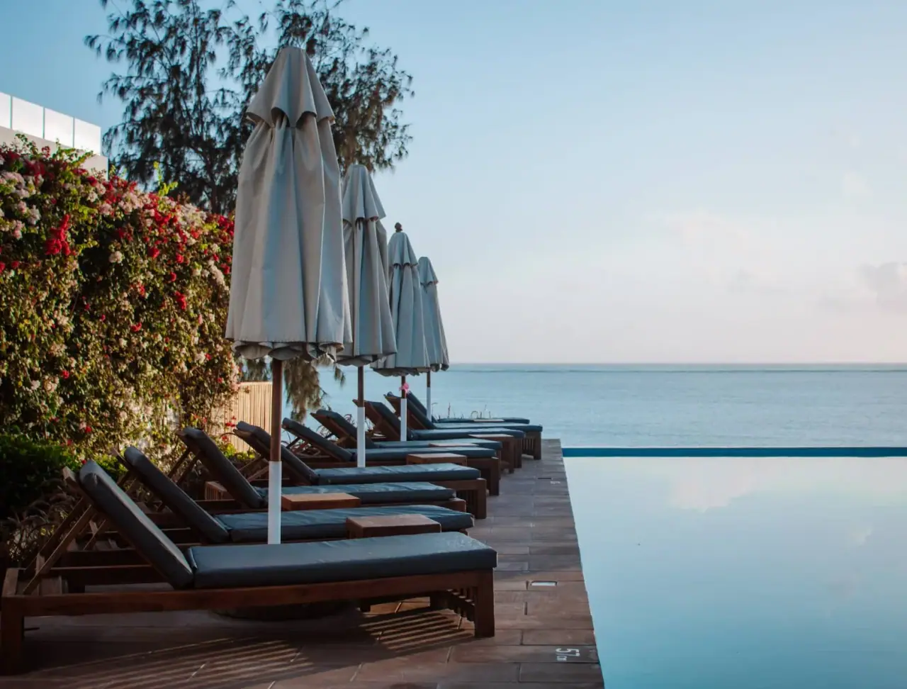 Row of poolside sun loungers and umbrellas along the infinity pool edge at dusk, Nungwi Dreams By Mantis