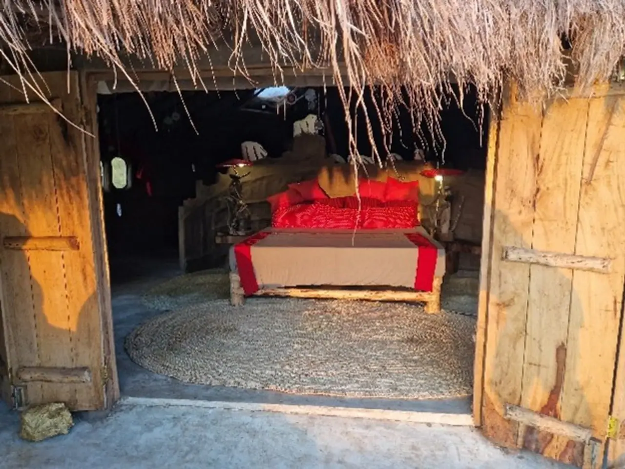 Kisiwa Boma suite bed with red linens beneath a thatched roof at Original Maasai Lodge