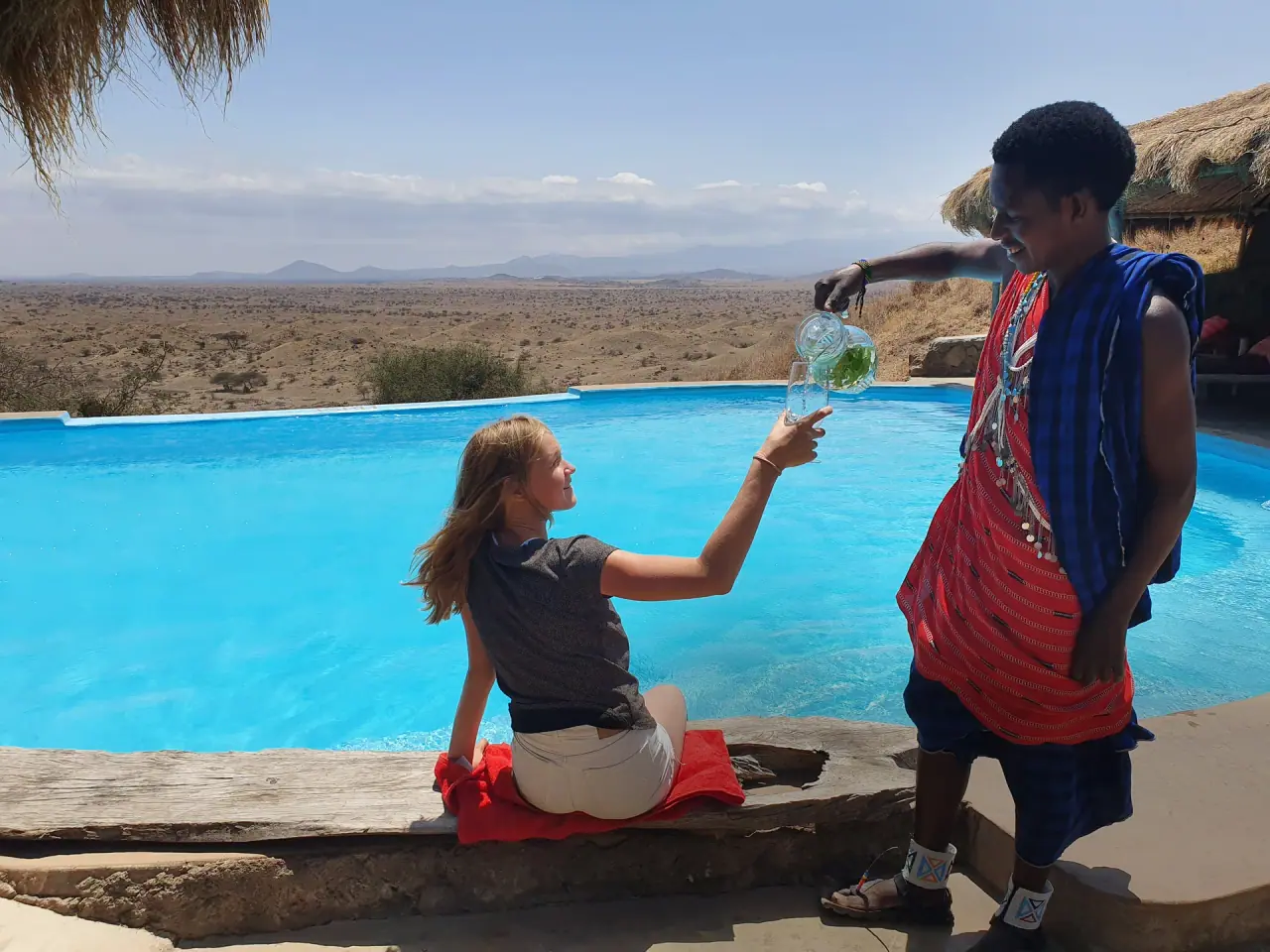 Guest receiving a poolside drink from Maasai staff overlooking the plains at Original Maasai Lodge