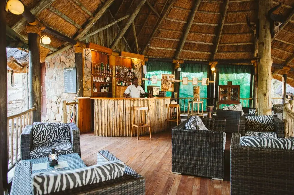 Thatched bar area with zebra-print seating and a bartender at Ruaha River Lodge