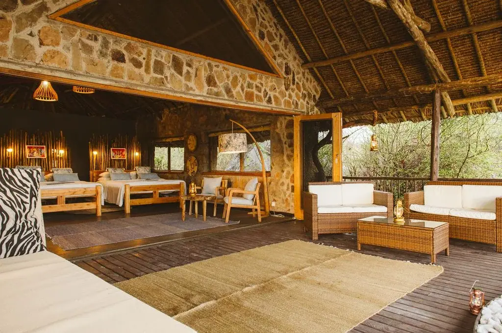 Stone-walled guest room lounge with twin beds and zebra-print cushions at Ruaha River Lodge