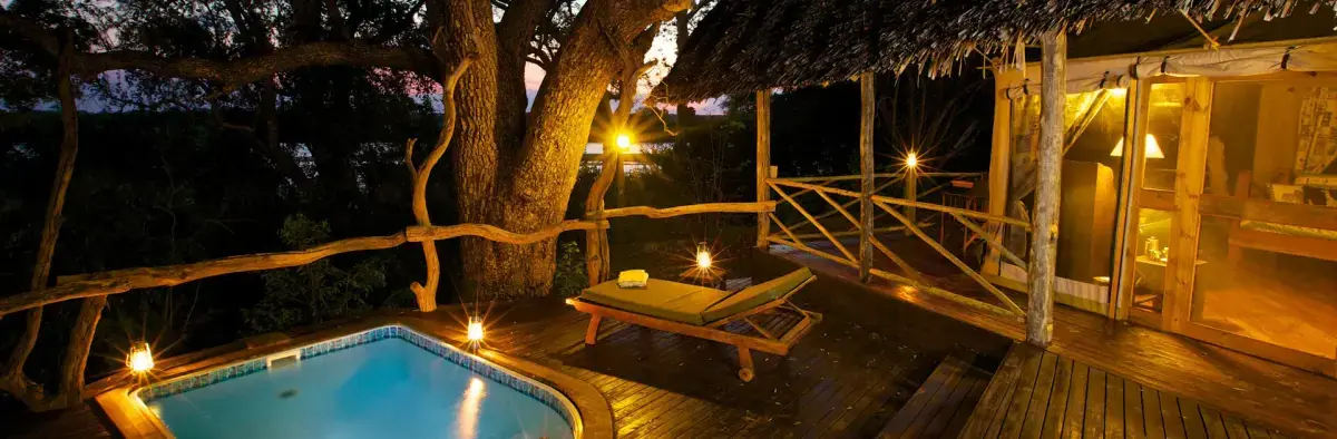 Private plunge pool and wooden deck lit at night beneath a giant tree at Rufiji River Camp