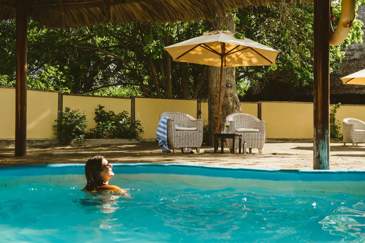 Guest swimming in the communal pool beneath a thatched umbrella at Rufiji River Camp