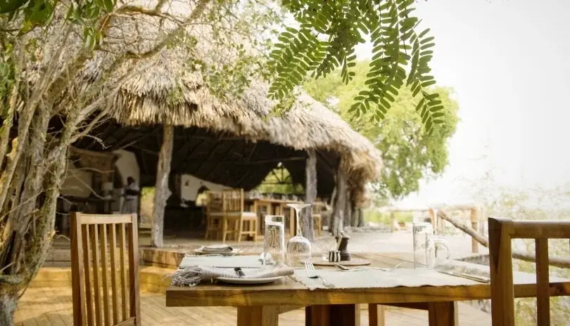 Outdoor dining table set on the thatched terrace at Sand Rivers Selous