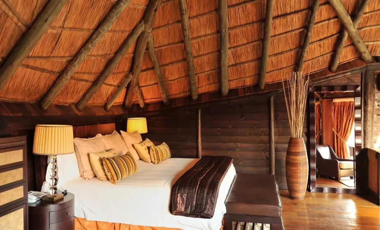 Guest room beneath a thatched roof with warm lamp lighting at Serena Mivumo River Lodge