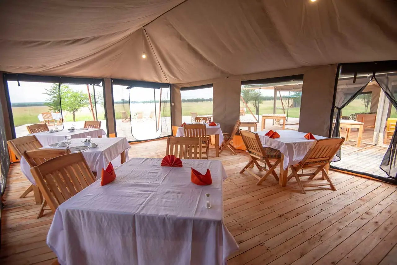 Open-sided dining tent at Serengeti Queens Camp set with white linens and folded orange napkins for breakfast