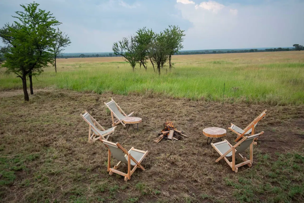 Camp fire circle with wooden safari chairs set on the central Serengeti plains at Serengeti Queens Camp