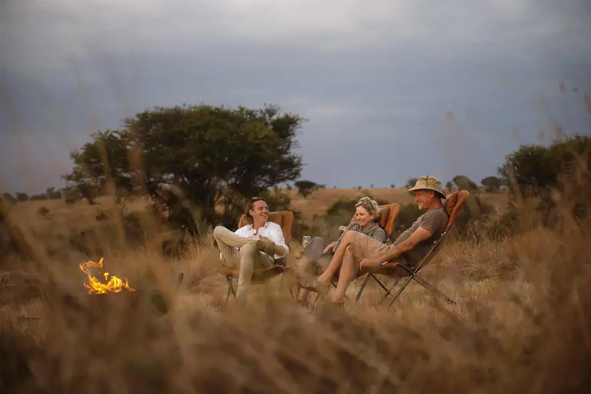 Guests relaxing around an open campfire on the Ndutu plains at dusk at Siringit Migration Camp