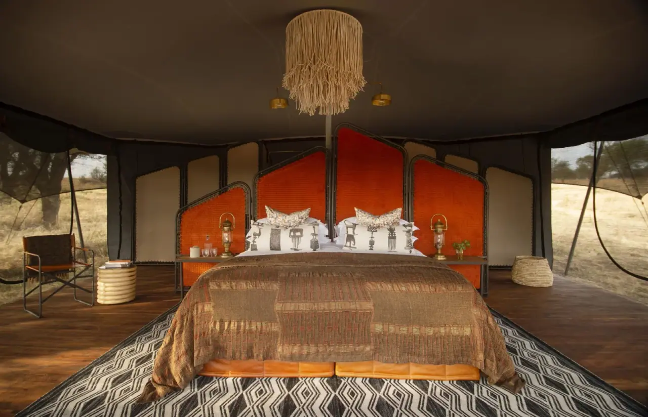 Tented bedroom suite at Siringit Migration Camp with a rust-orange leather headboard and patterned throw