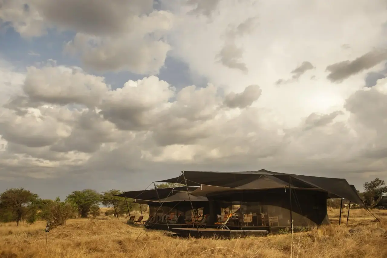 Mess tent exterior at Siringit Migration Camp, Ndutu site, under a dramatic cloudy sky on the open plains