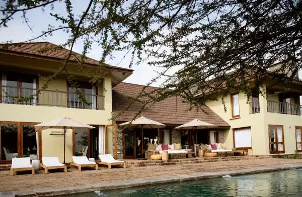 Exterior of Siringiti Arusha Villa with sun loungers and umbrellas beside the swimming pool