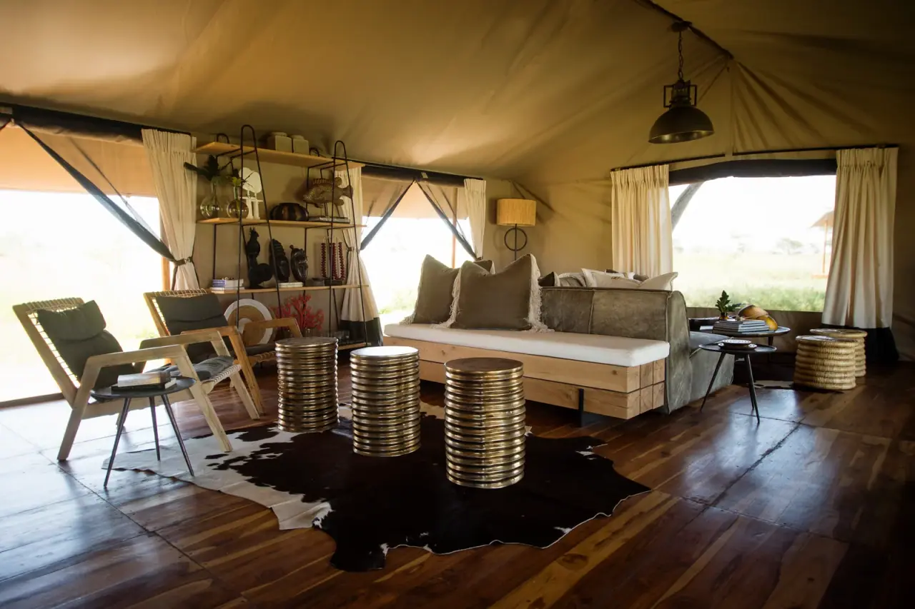 Lounge tent seating area at Siringiti Serengeti Camp with stacked brass side tables and a cowhide rug