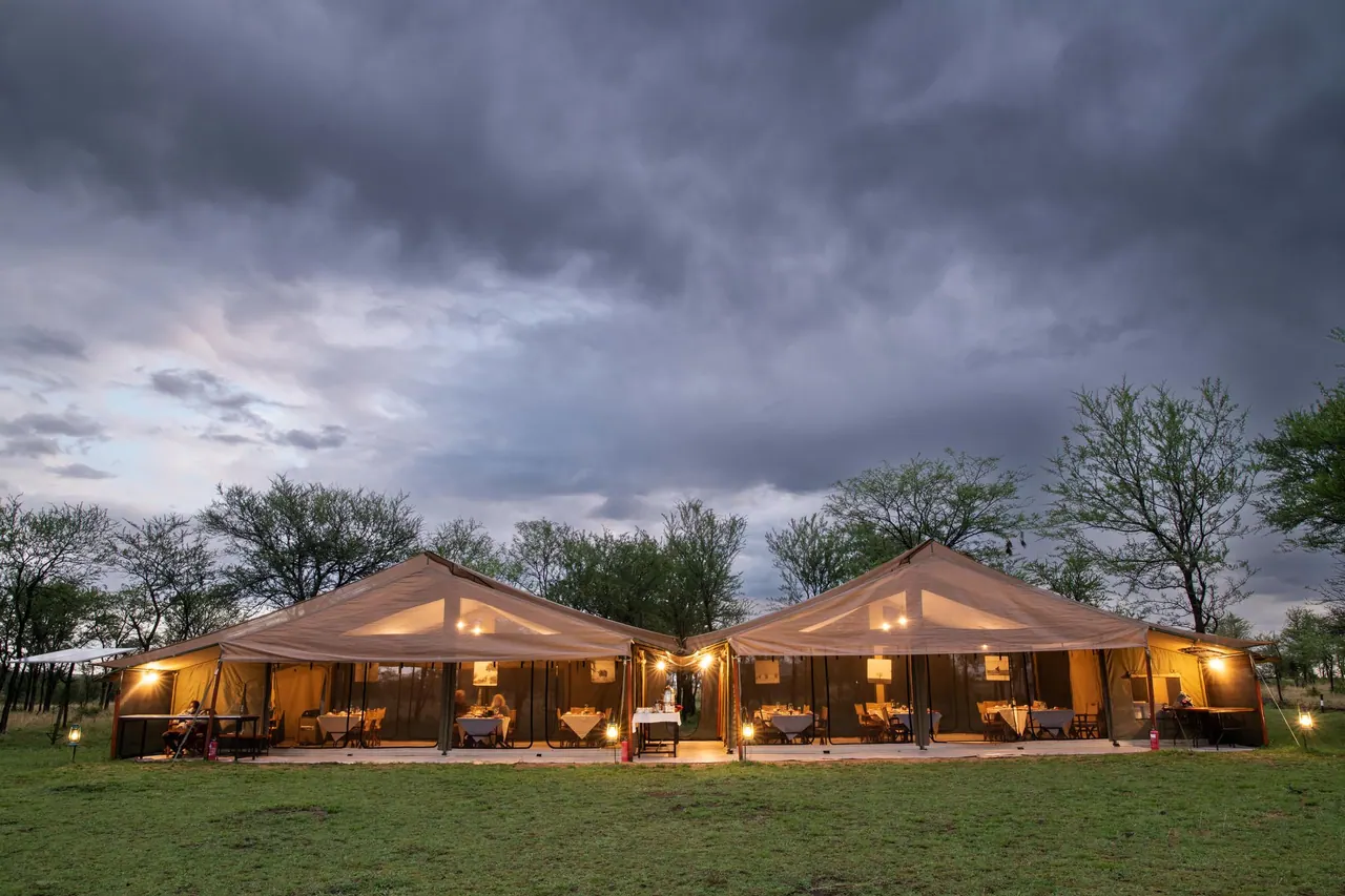 Two lit guest tents glowing at dusk under a stormy sky at Tarangire Katikati Tented Camp