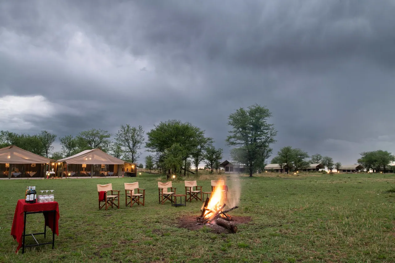 A campfire and director chairs on the lawn in front of the tents at Tarangire Katikati Tented Camp