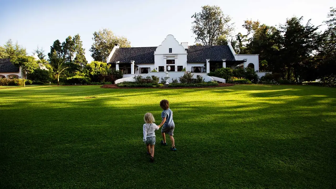 Children walking across the front lawn toward the white gabled manor house at The Manor at Ngorongoro