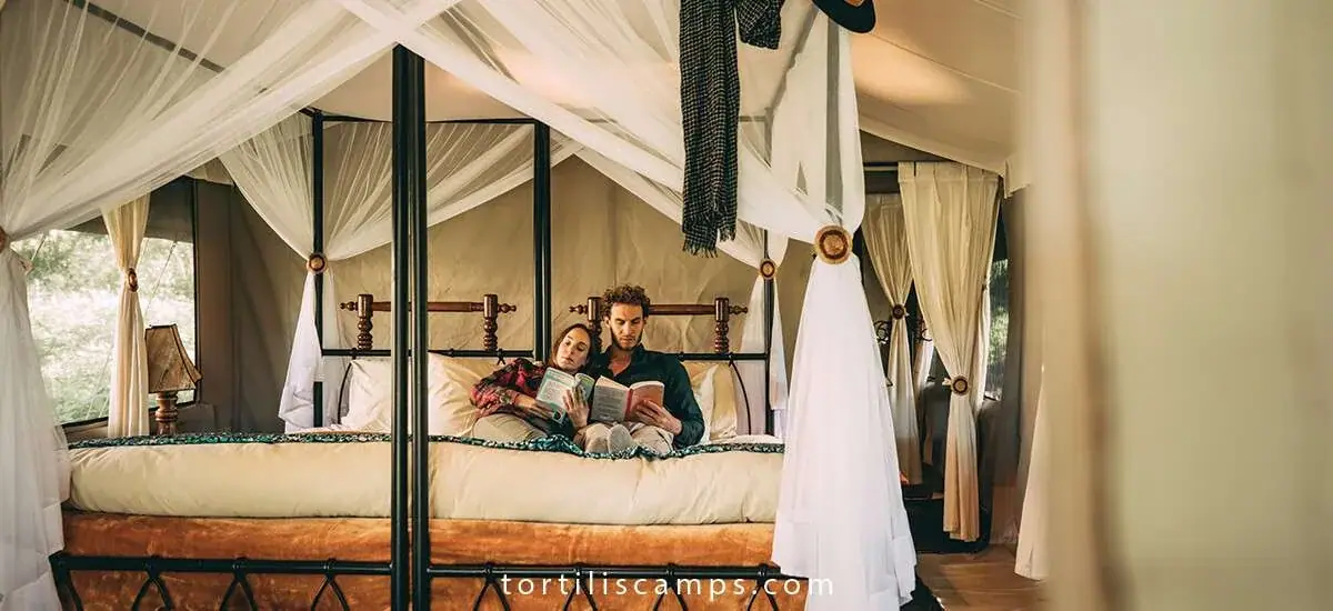 Couple reading together on a canopy bed draped in mosquito netting at Tortils Ngorongoro Camp