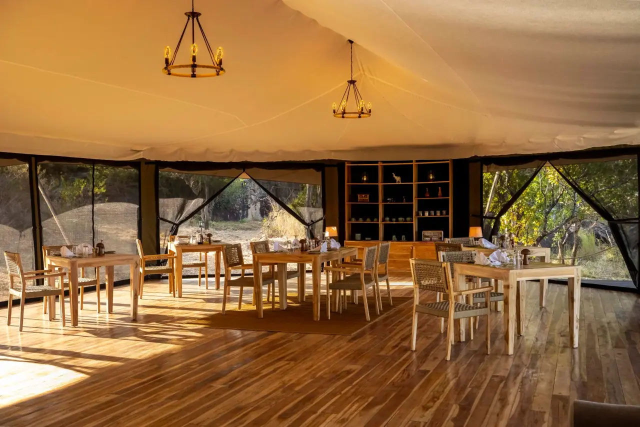 Open-air dining tent at Zuri Kilima Siri with wooden tables set beneath chandelier lighting