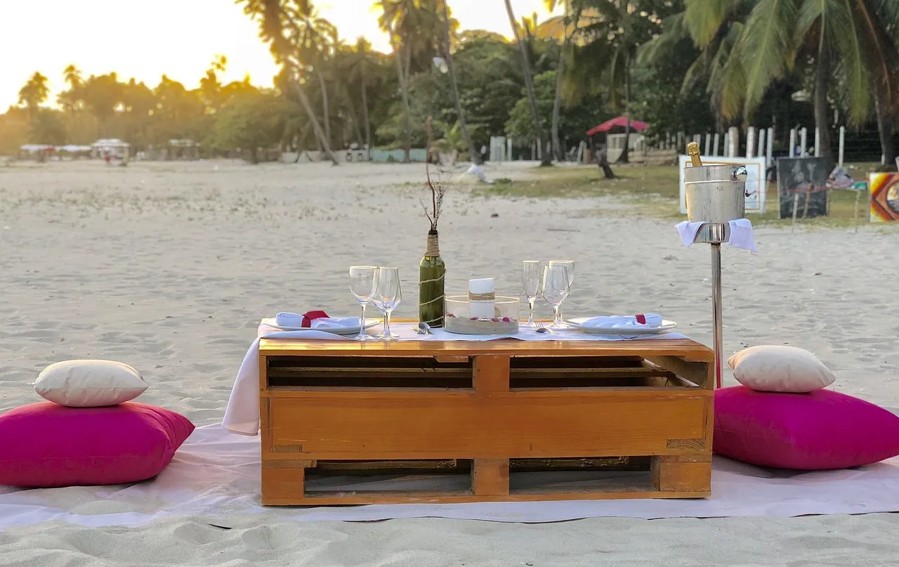 A low dining table set with glasses and cushions on a sandy beach