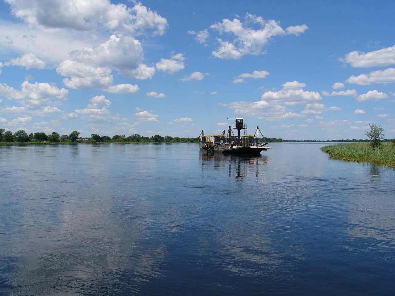 A boat on a wide, calm river under a bright sky