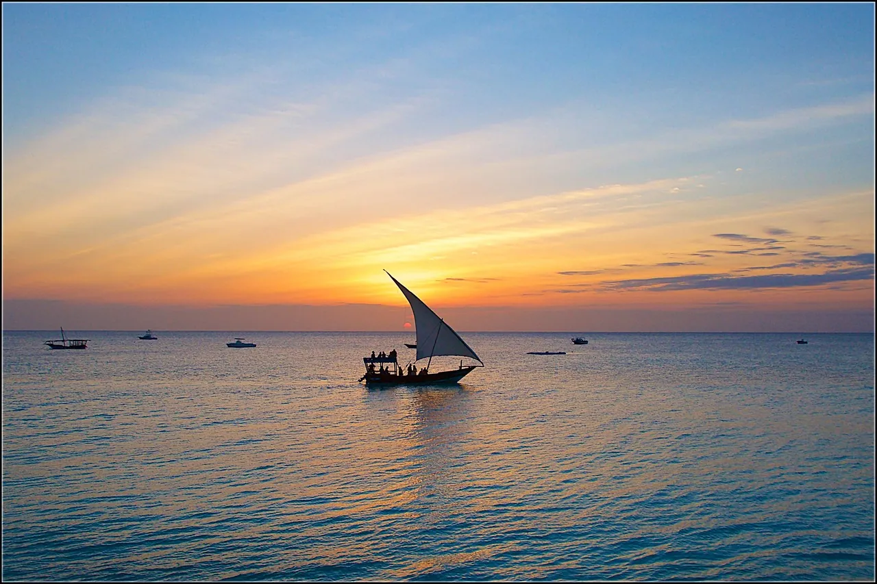 A wooden dhow sailing on calm water at sunset