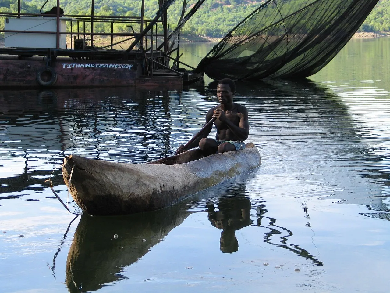 A man sitting in a wooden canoe on calm water