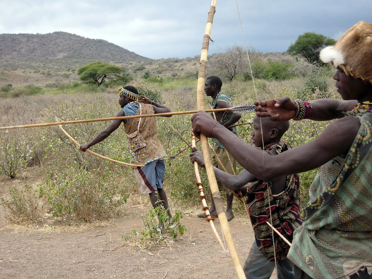Hadzabe hunters carrying bows through dry bush near Lake Eyasi