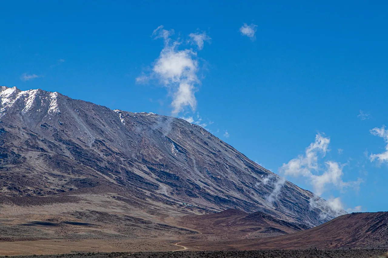 The glaciated slope of Kilimanjaro under a blue sky with drifting cloud