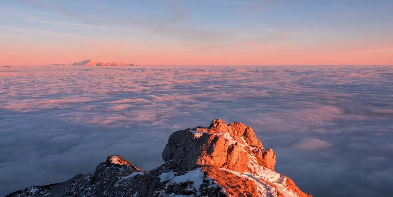 A rocky peak rising above a sea of pink cloud at sunrise