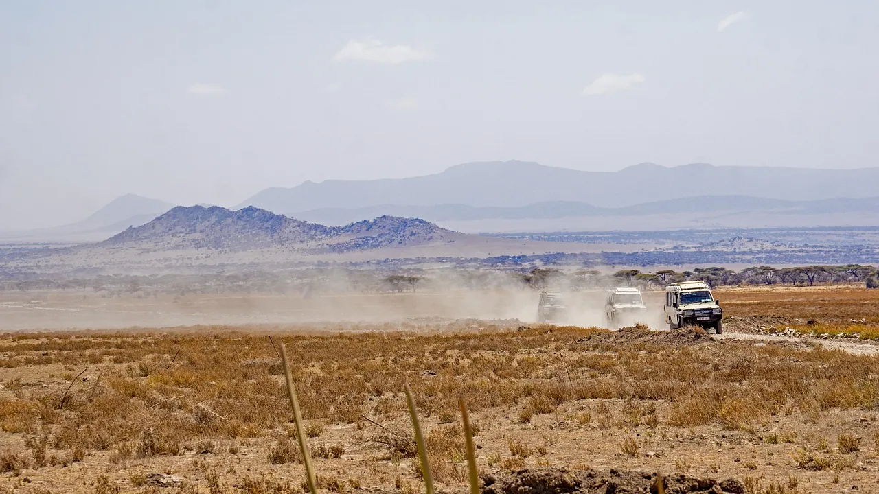 Safari vehicles raising dust across a dry open plain beneath distant hills