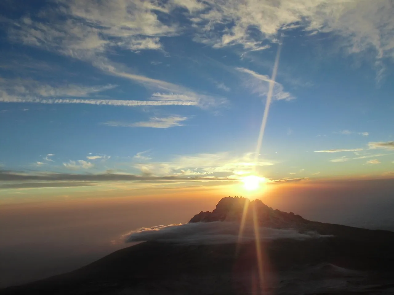 The sun bursting over a sea of cloud seen from a mountain ridge