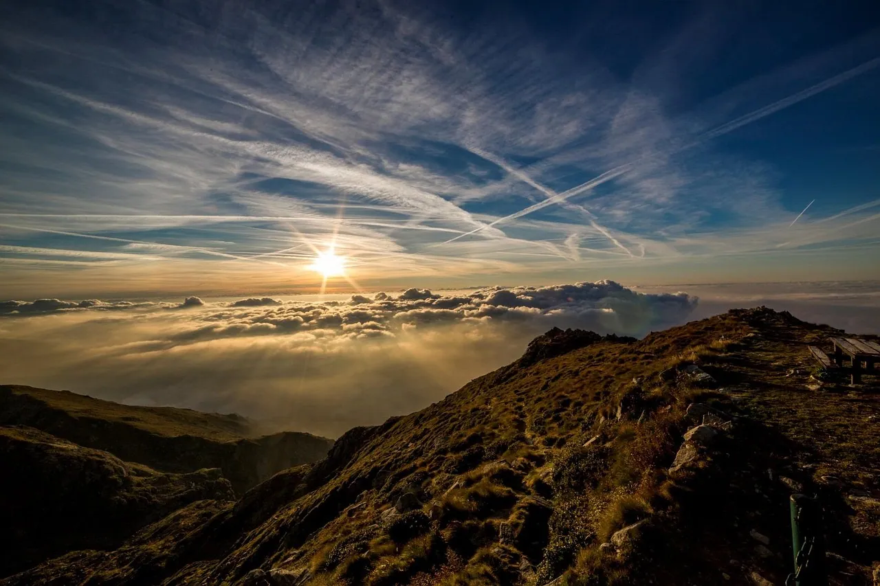 Sunrise flaring over a mountain ridge with high cloud streaks