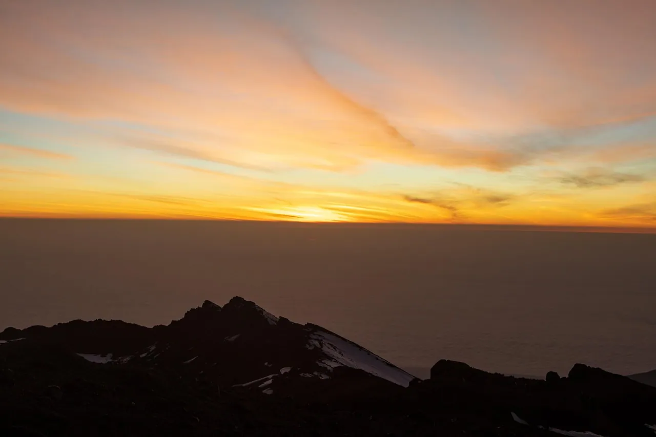 Sunrise glowing above the cloud line from a mountain ridge