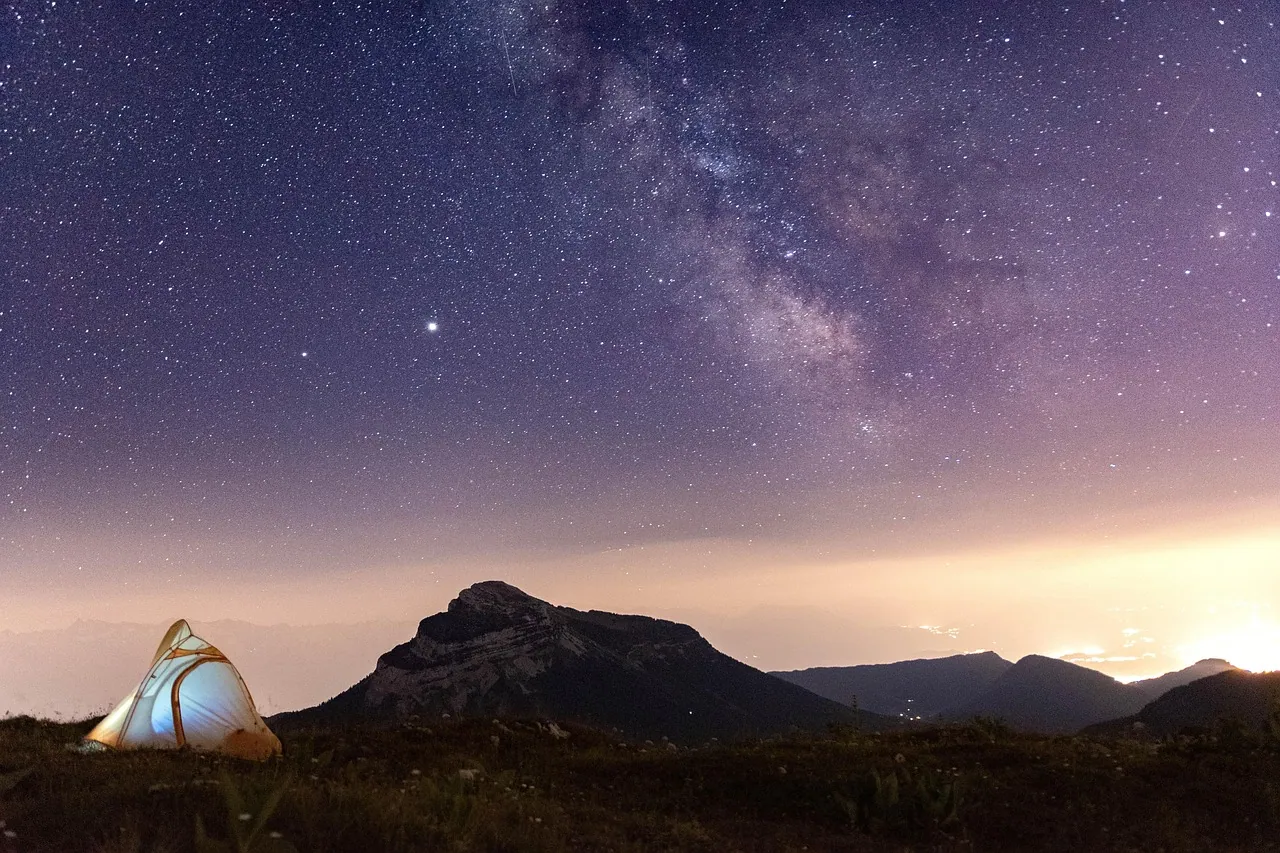 A small tent glowing beneath the Milky Way over a mountain ridge