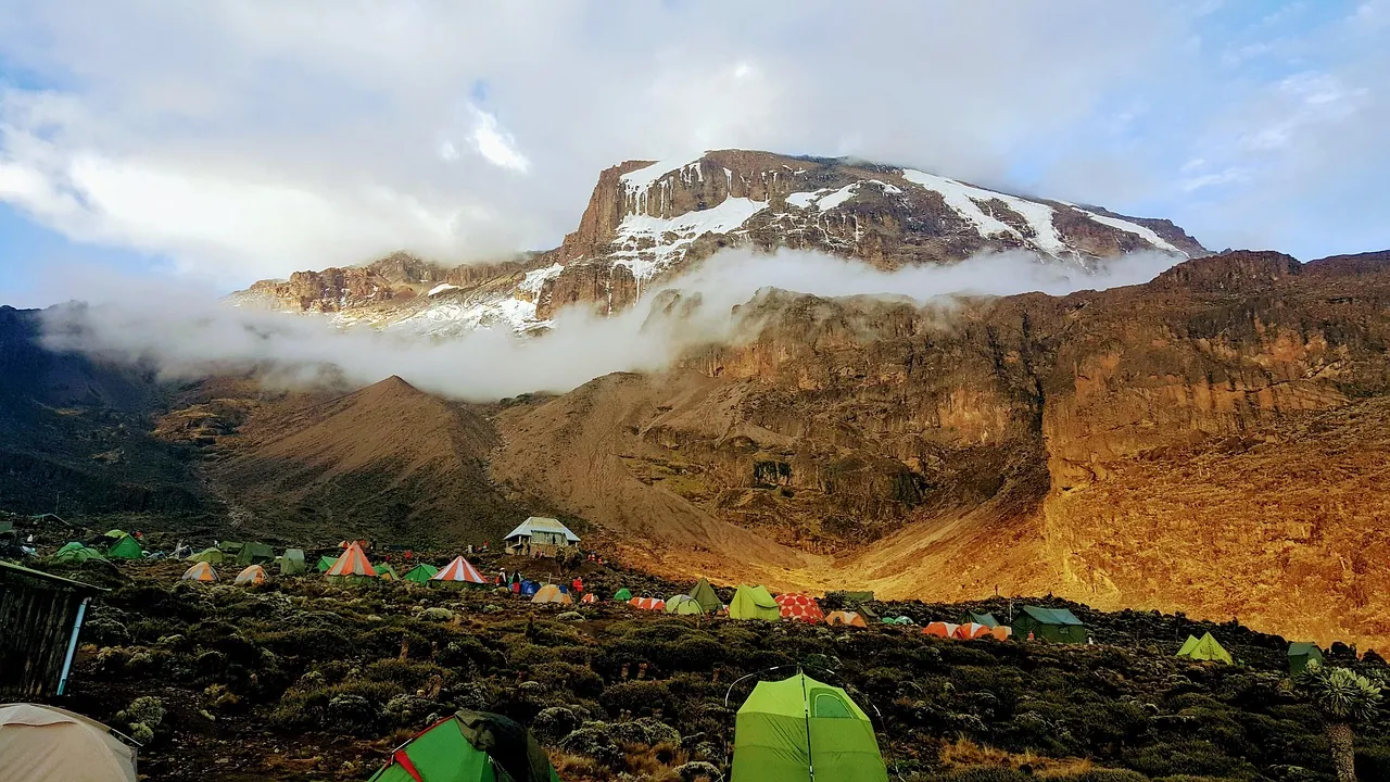 Tents pitched on a rocky mountain slope below a snow-streaked summit