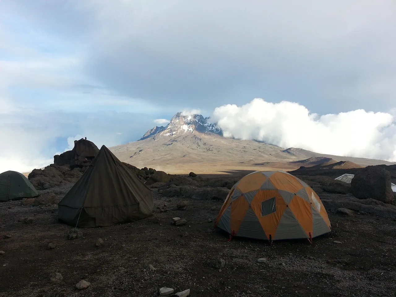 Mountain tents on rocky ground below the snow-streaked summit of Kilimanjaro
