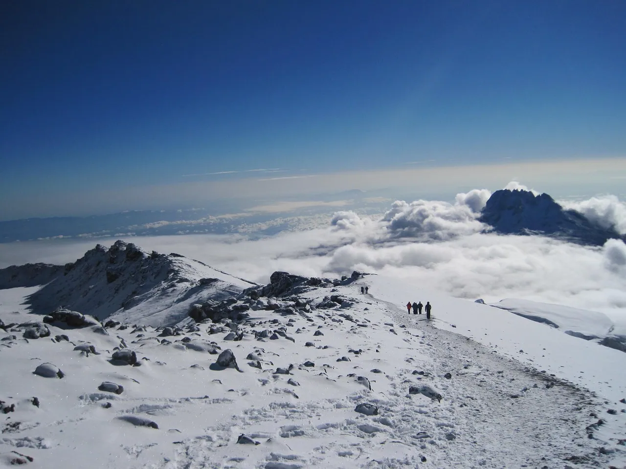Trekkers on a snowy ridge above the clouds