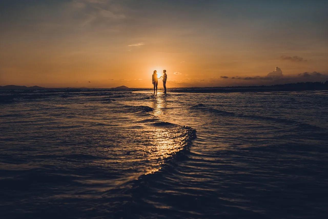 Two figures standing together at the water edge at sunset