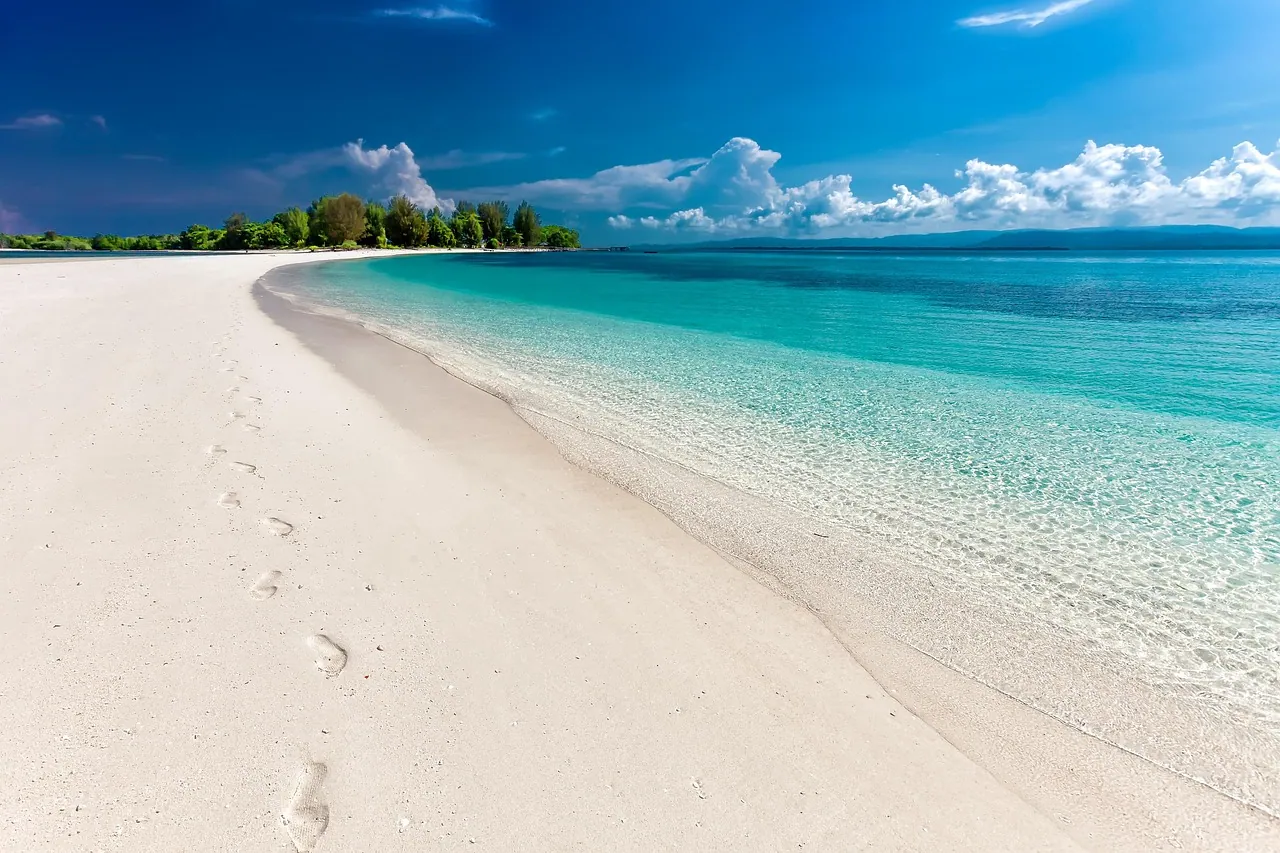 A white-sand beach with footprints beside turquoise water